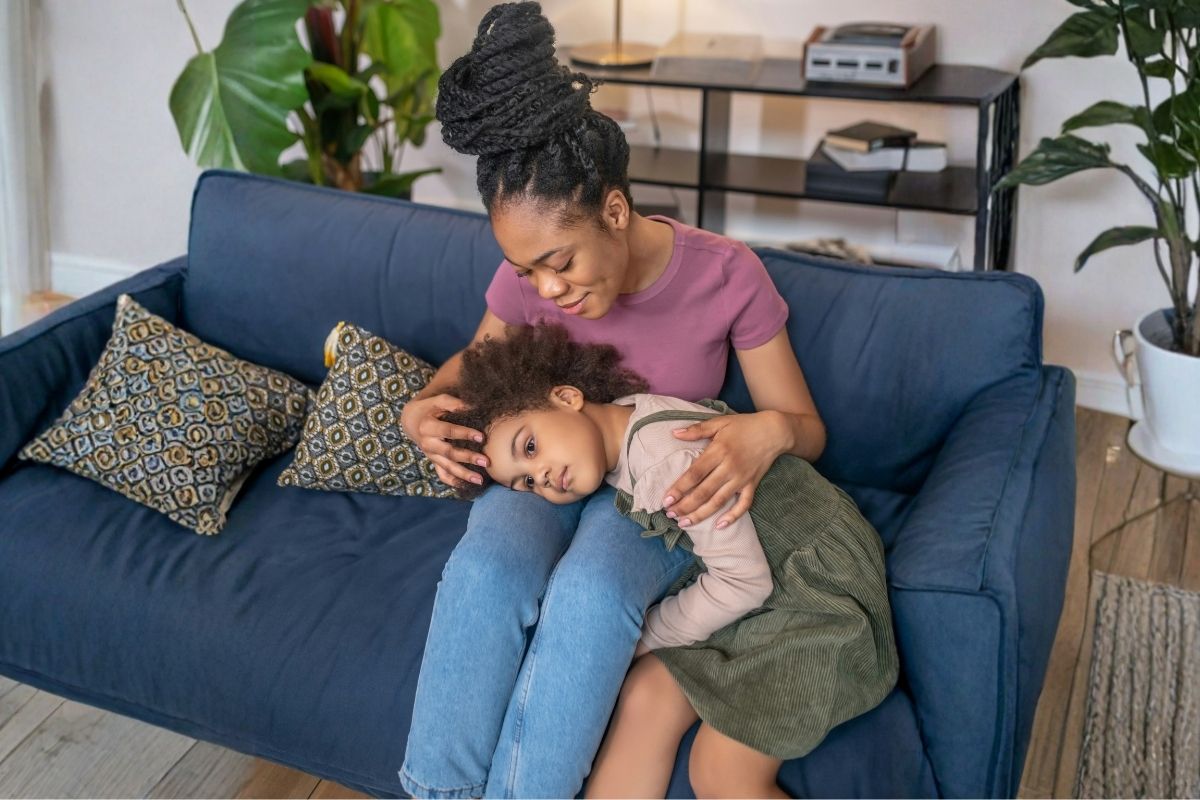 A child resting across a parent's lap on the couch after screen time.